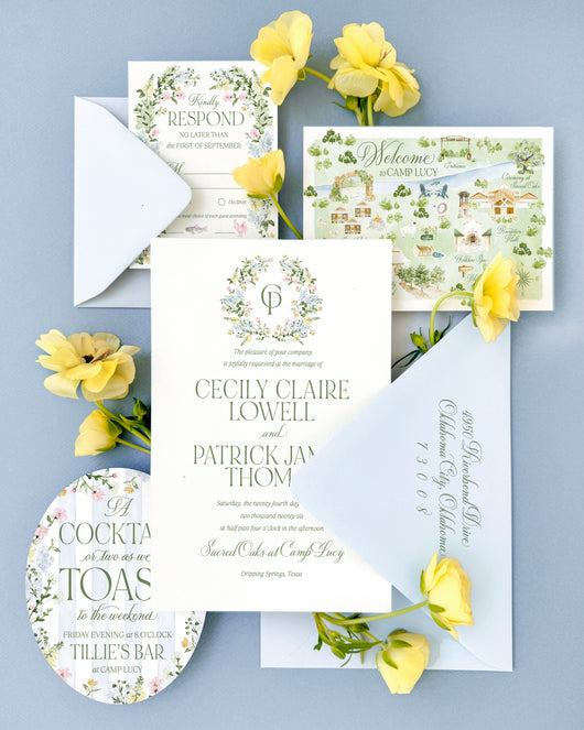 Luxury Camp Lucy wedding invitation suite featuring a custom watercolor wedding map of Camp Lucy in Dripping Springs, Texas, floral crest details, soft blue envelopes, and elegant fine art wedding stationery with garden-inspired elements.